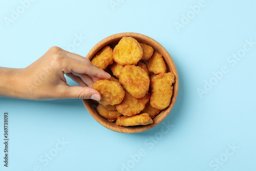 Φωτογραφία Female hand holds nugget over the blue background with bowl of nuggets