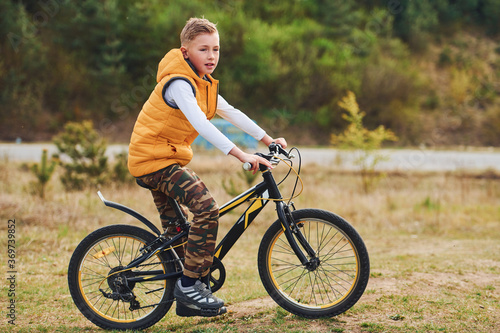 Young boy in orange colored jacket sitting on his bike outdoors at daytime