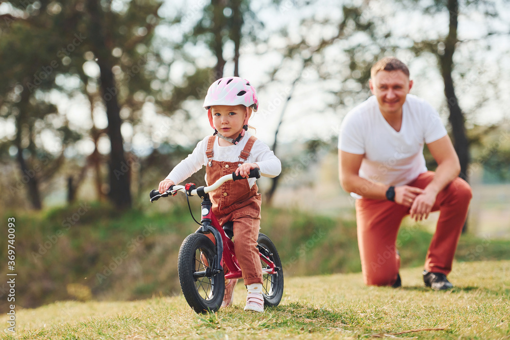 Father in white shirt teaching daughter how to ride bicycle outdoors