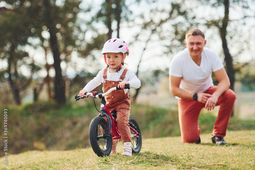 Father in white shirt teaching daughter how to ride bicycle outdoors Father in white shirt teaching daughter how to ride bicycle outdoors