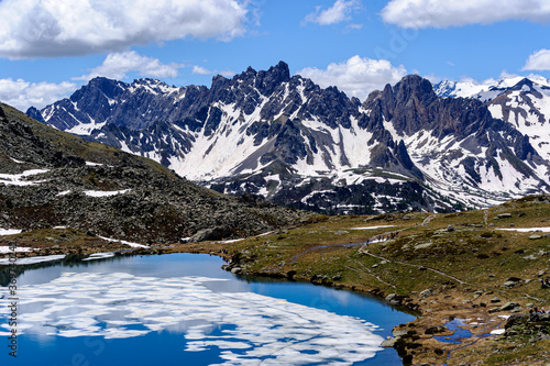 High-altitude lake still covered with ice. In the background a grey mountain range and a beautiful blue sky.