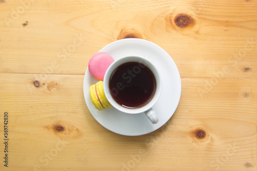 Top view of macaron and tea in white mug on wooden background.