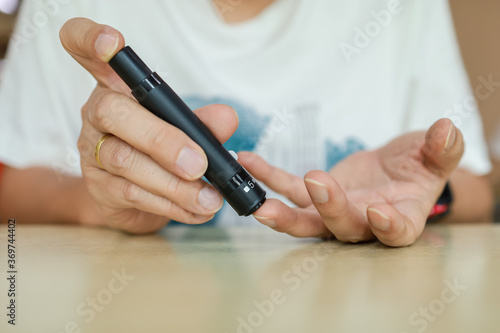 Close up of man hands using lancet on finger to check blood sugar level by Glucose meter. Use as Medicine  diabetes  glycemia  health care and people concept.