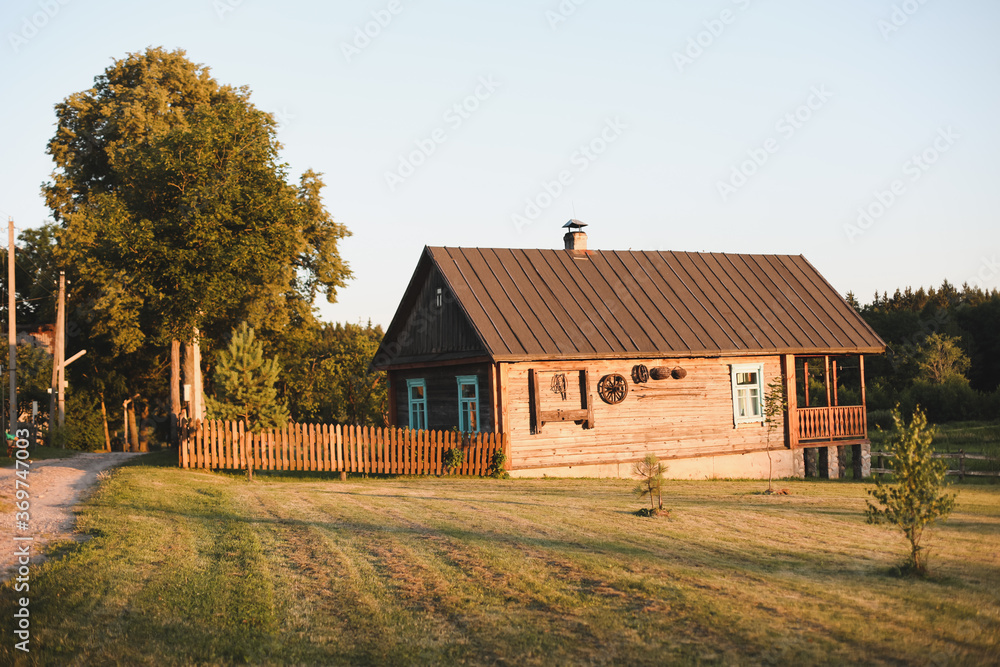 Fototapeta premium old wooden house in village. Farmhouse in Belarus. View of rustic ethnic house on sunset. rural landscape