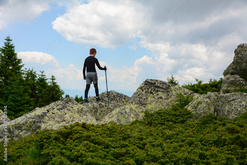 Gesture of triumph. Satisfy hiker in black shirt and grey trousers. School boy on the peak of cliff watching down to landscape.