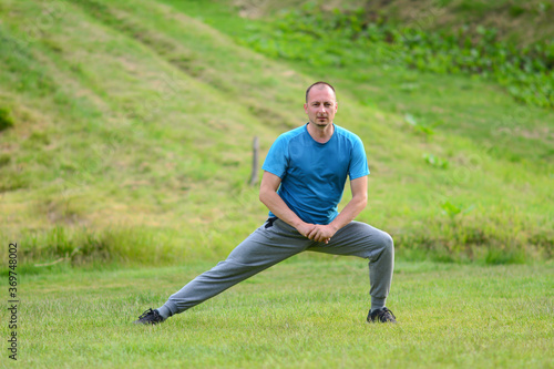 Handsome man stretching leg and warming up for training. Athletic young man stretching after run in nature. Fit man doing stretching exercises outdoors.