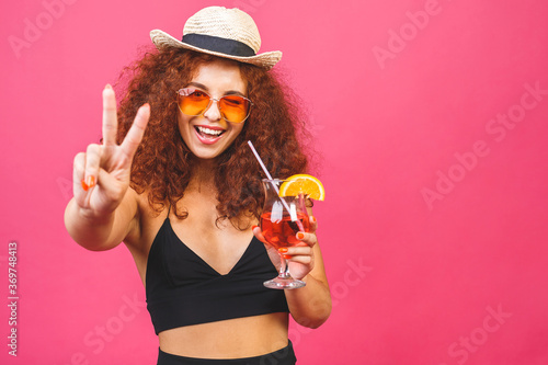 Happy beautiful woman in summer casual clothes with a glass of cocktail drink studio shot isolated on colorful pink backgroud.