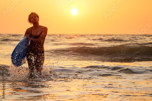 afro american woman run with surfboard on beach in Goa