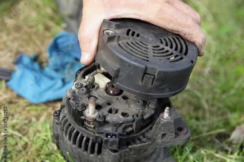 Canvas Print Used car 12 V alternator with back cover removed close up in hand on green grass