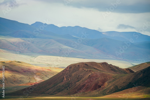 Fantasy vast landscape with vivid multicolor mountains in sunlight. Magenta rocky hill in scenic mountain valley. Colorful sunny scenery with multi-color mountains. Awesome picturesque mountain relief