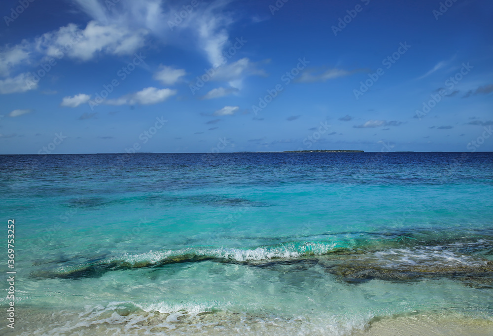 Waves of the Indian ocean against the blue sky with white clouds in the Maldives