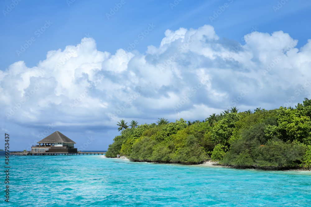 Vibrant blue ocean and white clouds over palms and bungalow in Maldives.