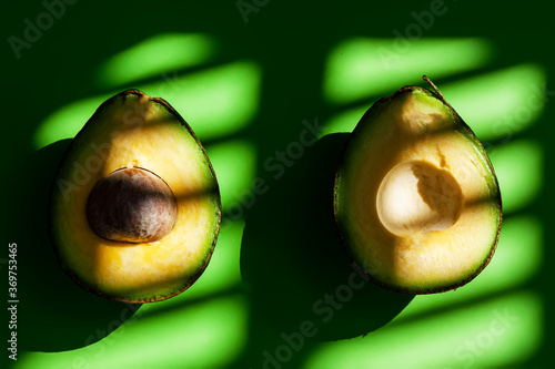 Fresh ripe avocado cut in half on the green background with shadows of natural sun light. Antioxidant snack and healthy eating concept. Space for text photo