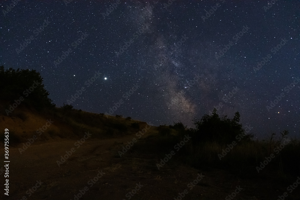 The milky way over the road. Beautiful night landscape with starry sky. The planet Saturn and Jupiter on the background of the milky way. Stargazing in the summer.