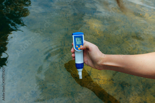 A woman's hand holds a waterproof tester pen and measures the total concentration of dissolved salts (TDS) and the temperature in the river. People, science concept. 