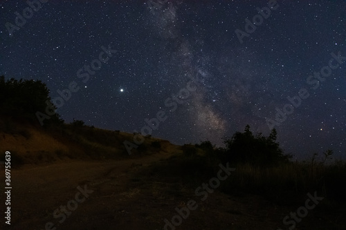 The milky way over the road. Beautiful night landscape with starry sky. The planet Saturn and Jupiter on the background of the milky way. Stargazing in the summer.