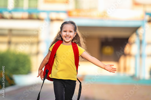 Schoolgirl elementary. little girl with backpacks runs from school. A happy child is happy to return to school. beginning school year. Children are happy to run to school. education.