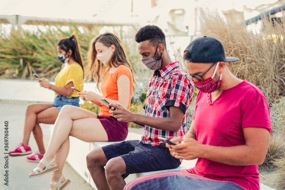 Obraz premium Friends using their smartphones in covid 19 times protected with face mask - Young people using mobile device in distance outdoors