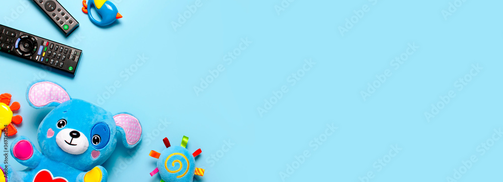 Black TV audio remote control and baby toys rattles, toy puppy on blue background flat lay top view copy space. Concept of viewing children's television shows, cartoons, children's films. Home leisure Black TV audio remote control and baby toys rattles, toy puppy on blue background flat lay top view copy space. Concept of viewing children's television shows, cartoons, children's films. Home leisure