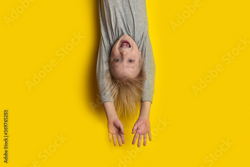 Foto Surprised fair-haired boy hanging upside down with arms outstretched