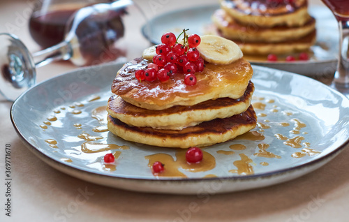 Fresh homemade pancakes with red currants and caramel on gray plate and craft background with black and strong coffee. Delicious breakfast and pastries.