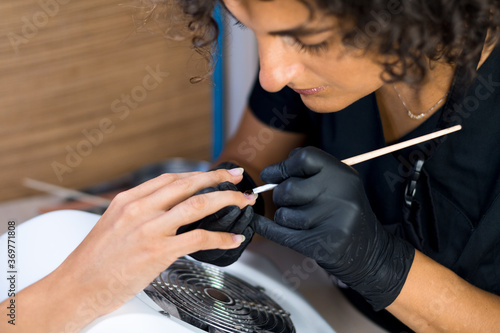 manicurist master in black gloves doing nail polishing with a brush in the spa salon