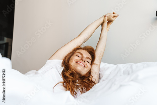 Image of woman stretching her body while lying in bed after sleep photo