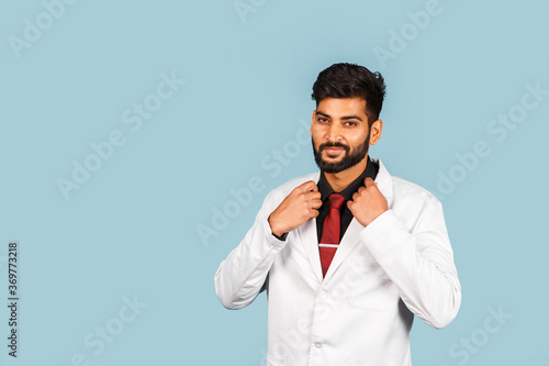 Handsome modern indian / asian doctor with stethoscope, tie and white coat on blue background