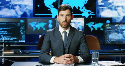 Caucasian handsome man in suit and tie sitting at table and talking to camera like news reporter. Male spokesman telling about digital security on TV. Government representative having speech.