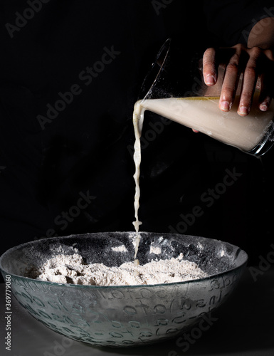 Hand dropping water over a bowl with flour on a black background