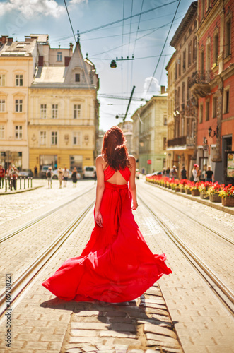Passionate young girl, lady in long red dress on street of an old European city