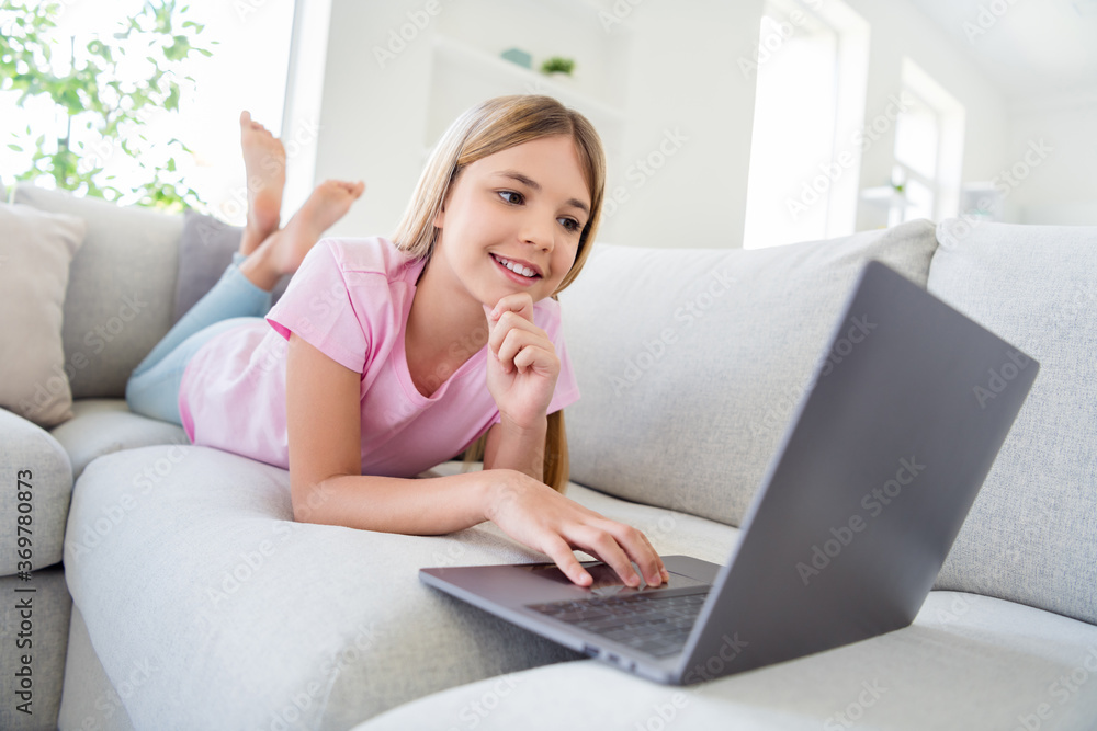 Full length photo of positive girl kid study remote use laptop have online project chatting communication with teacher classmates lying divan in house indoors Full length photo of positive girl kid study remote use laptop have online project chatting communication with teacher classmates lying divan in house indoors