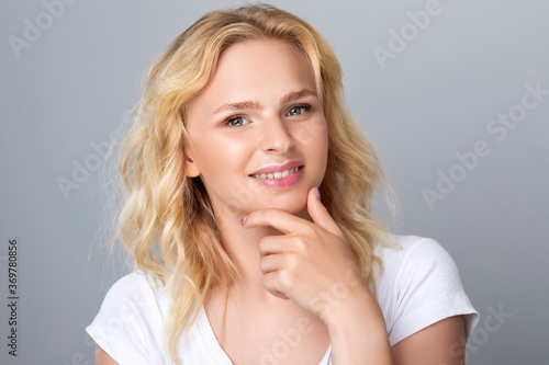 Beautiful smiling blonde woman with curly hair, clean skin and fresh make-up. She has beautiful blue eyes. Aesthetic cosmetology, hair treatment and makeup concept.