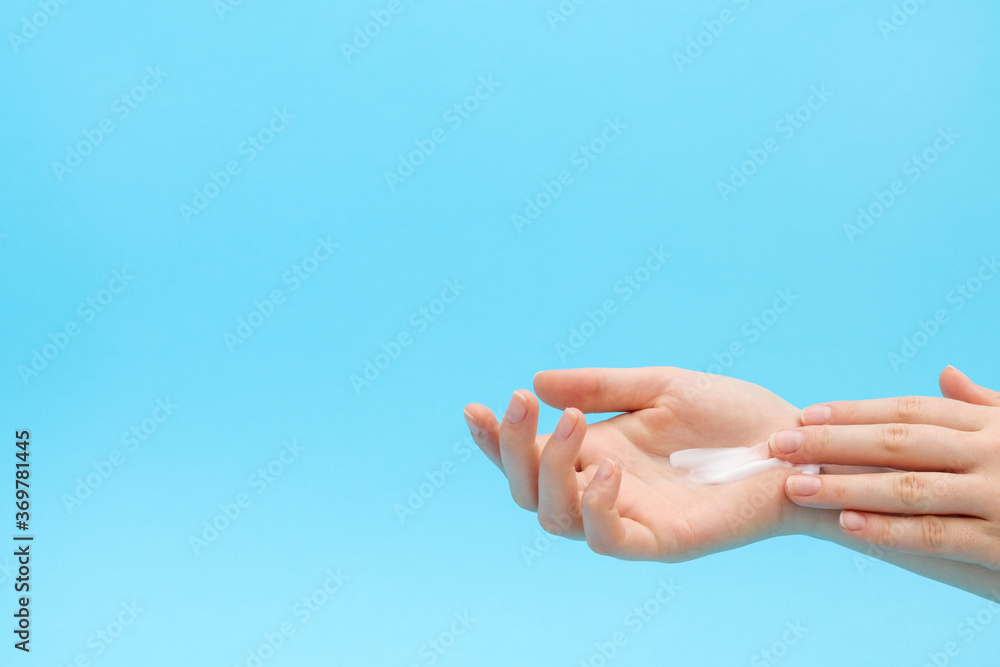 Woman applying organic cream on hand. Blue background. Right hand with cream.