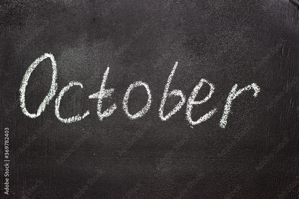 Fototapeta premium Month written in white chalk on a chalkboard. The month depicted on the chalkboard is October
