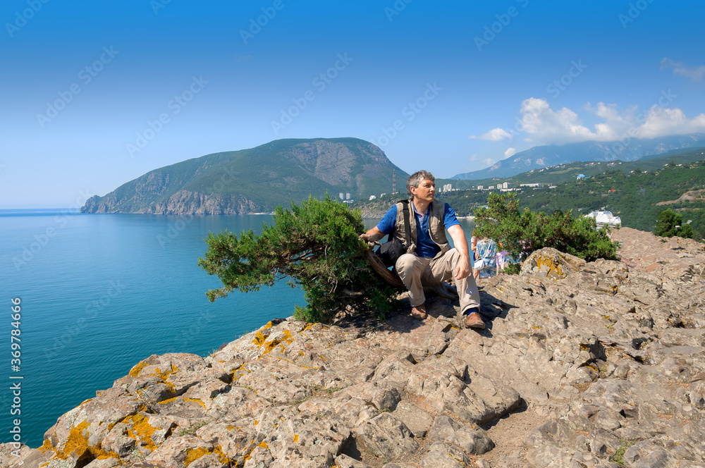 A man of pre-retirement age sits on a rock above the sea.