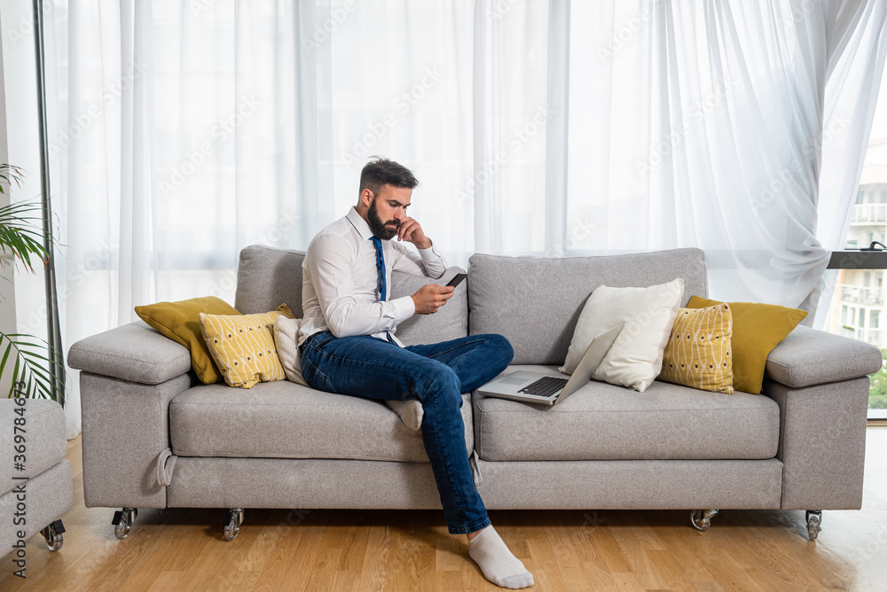 Young freelancer business man sitting on sofa at his home and taking a break on his phone of laptop and waiting for his boss to talk about new business project as freelance worker Young freelancer business man sitting on sofa at his home and taking a break on his phone of laptop and waiting for his boss to talk about new business project as freelance worker