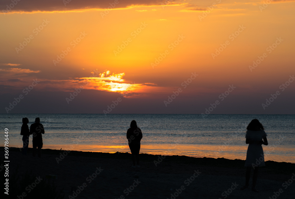 Tourists at sea on the beach, admire the sunrise. Silhouettes of people