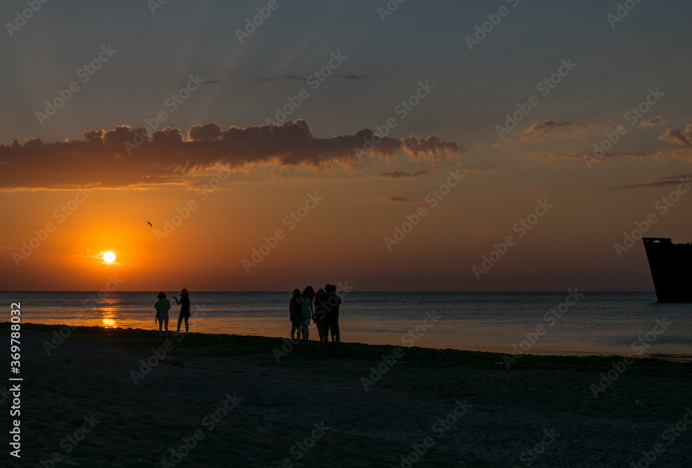 Tourists at sea on the beach, admire the sunrise. Silhouettes of people