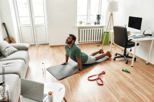 Young active man looking focused while exercising, practicing yoga during morning workout at home. Sport, healthy lifestyle