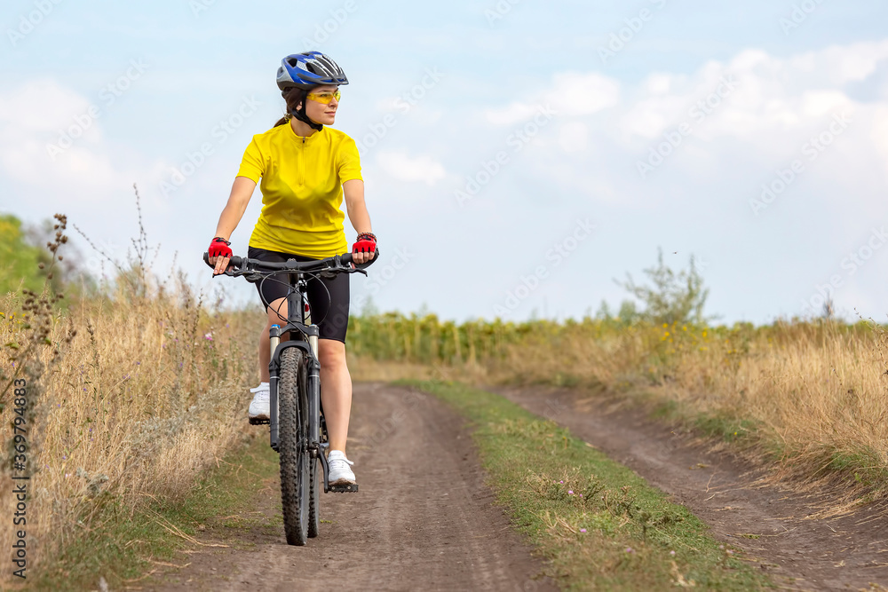 Fototapeta premium beautiful and happy girl cyclist rides a bicycle on the road in nature. Healthy lifestyle and sports. Leisure and hobbies
