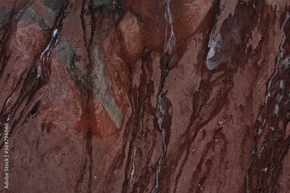 Abstract view of a small gletser with meltwater at a cliff that has different shades of red and grey and a small amount of snow