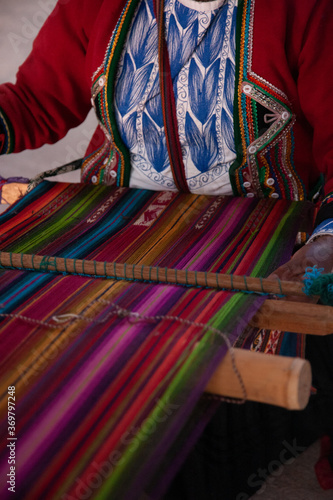 A colorfull andean cloth or rug being woven by a woman in a typically indigenous dress