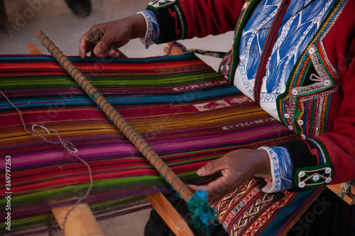 An indigenous dressed woman in the andes that is weaving a colorful typical rug