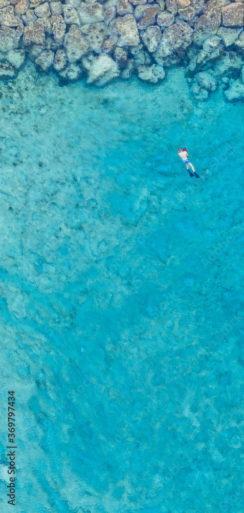 An aerial view of the beautiful Mediterranean Sea and a swimmer, where you can see   the cracked rocky textured underwater corals and the clean turquoise water of Protaras, Cyprus, 