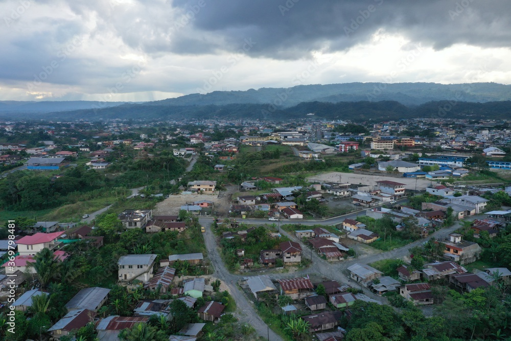 Aerial view of a small city  with many tin roofs and surrounded by rainforest and mountains and dark clouds