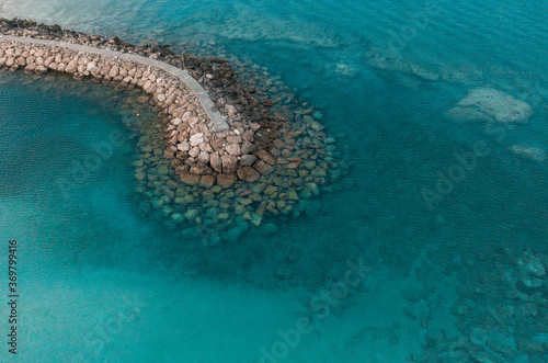 An aerial view of a beautiful walkway surrounded by rocks in the Mediterranean sea, where you can se the rocky textured underwater corals and the clean turquoise water of Protaras, Cyprus 