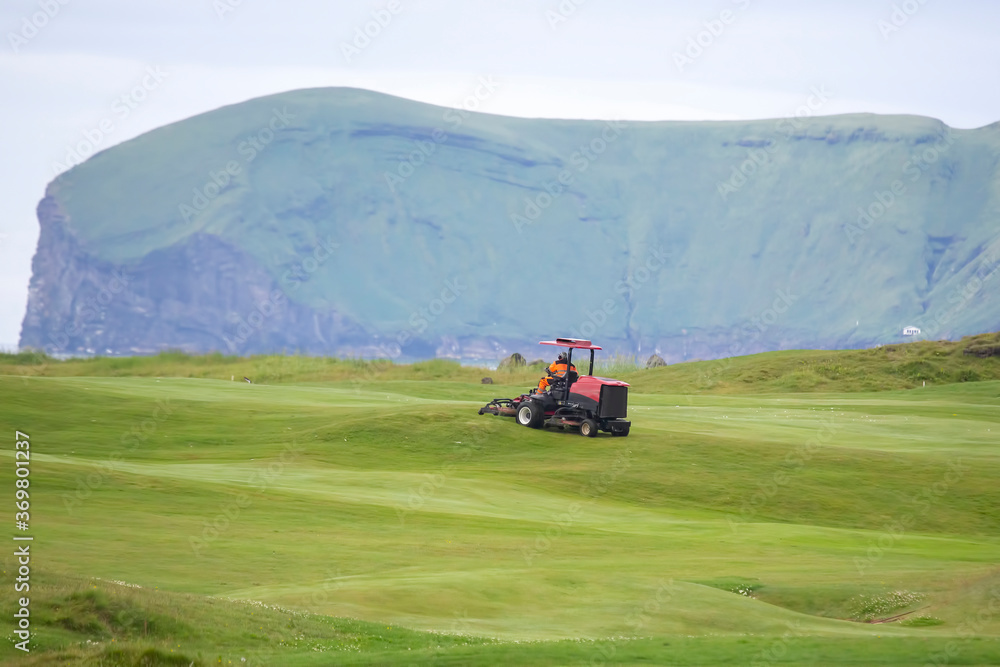 man rides on a special machine to clean the grass of the Golf course man rides on a special machine to clean the grass of the Golf course