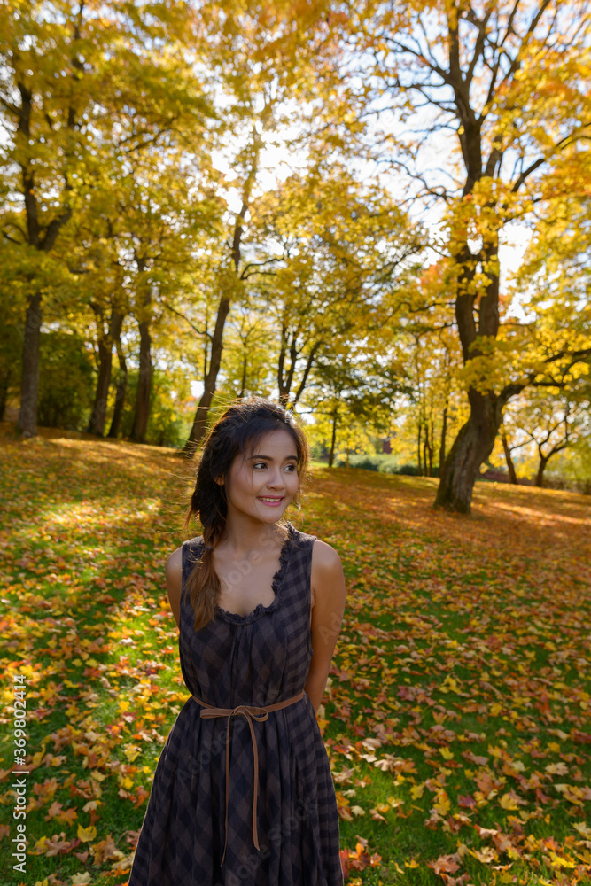 Young happy Asian woman smiling and thinking surrounded by scenic autumn trees in the forest Young happy Asian woman smiling and thinking surrounded by scenic autumn trees in the forest