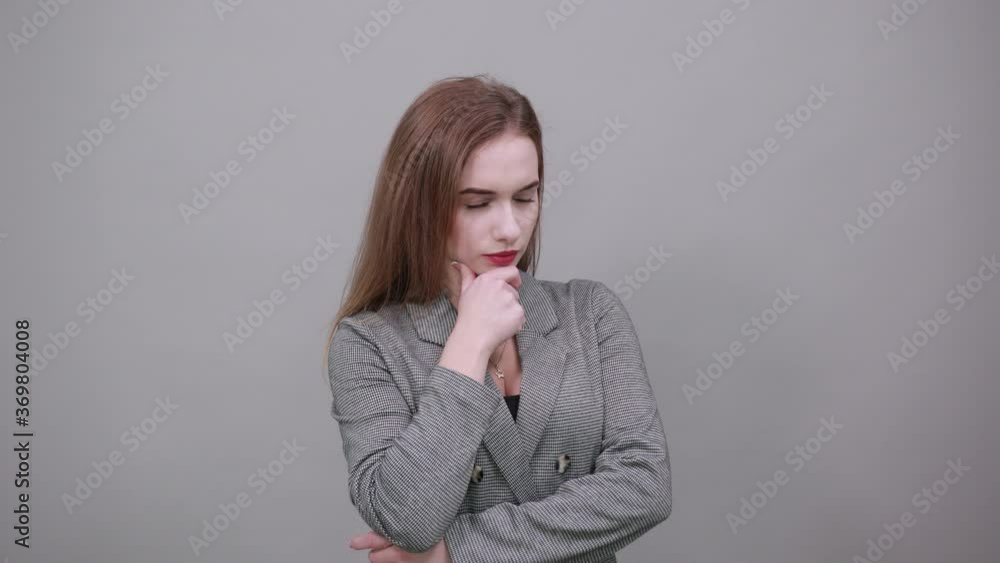 Hand on chin thinking about question, pensive expression. Doubt. Thoughtful face. Using that incredibly sharp business mind. Young attractive woman, dressed gray jacket, with green eyes, light brown Hand on chin thinking about question, pensive expression. Doubt. Thoughtful face. Using that incredibly sharp business mind. Young attractive woman, dressed gray jacket, with green eyes, light brown